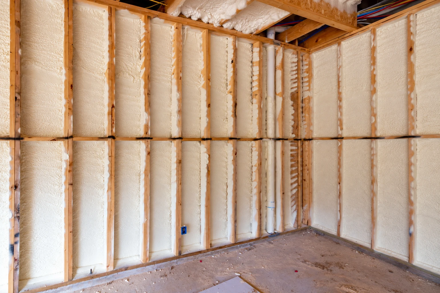 Closed-cell foam insulation fills the exposed wall cavities of a framed room.
