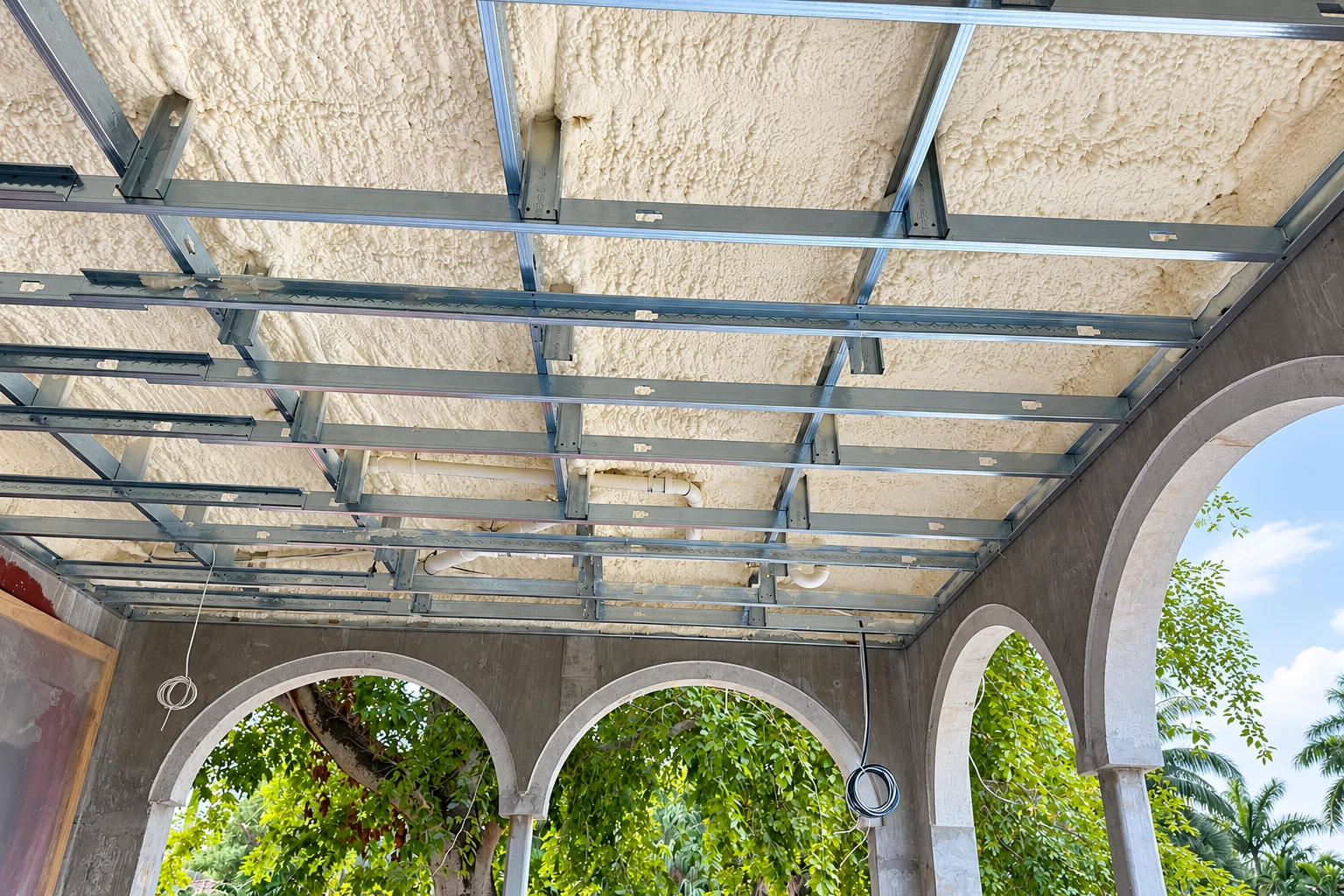 Cream spray foam covers the ceiling of a commercial space framed with metal supports and arched openings.