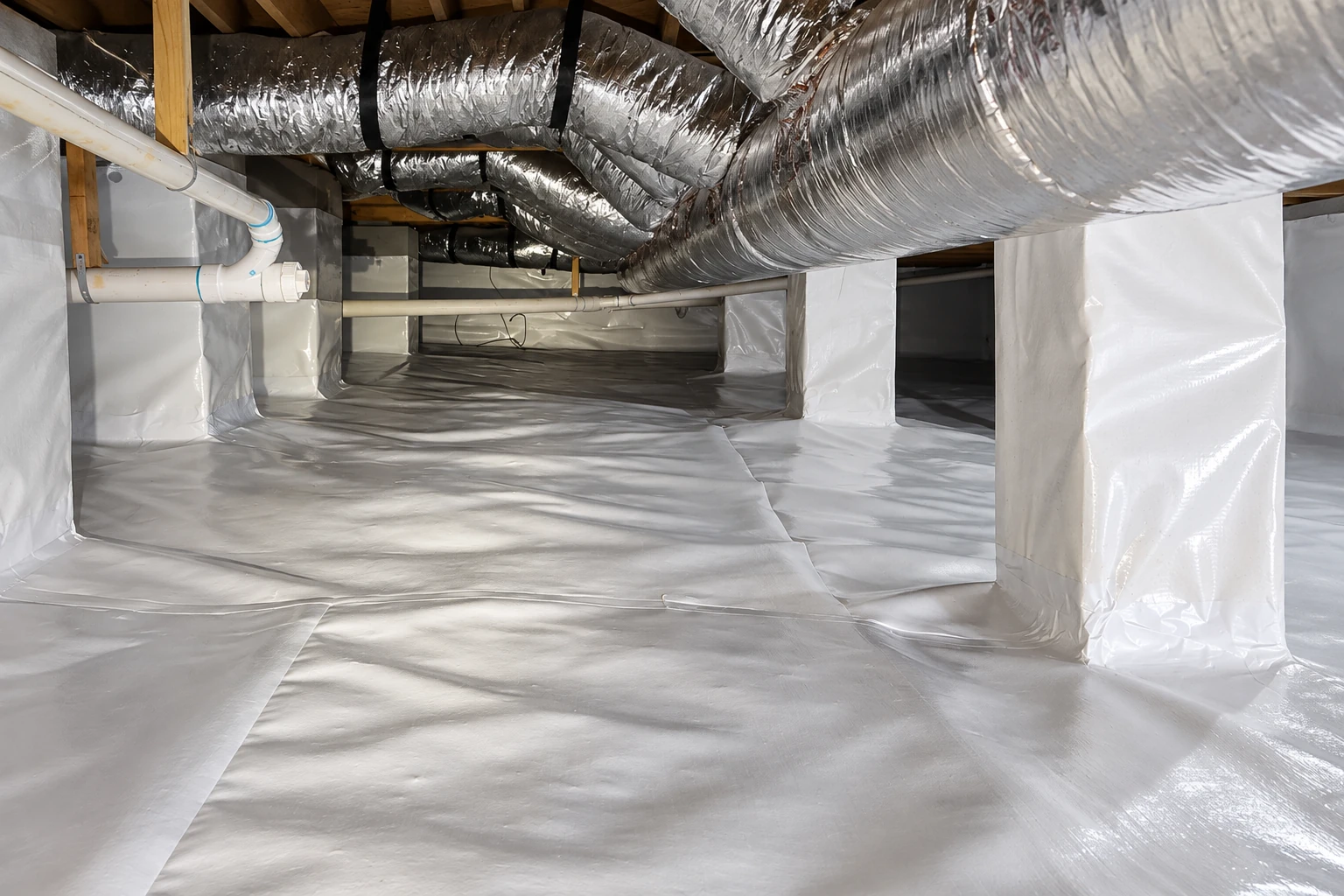 A crawl space floor and support columns are covered with a reflective white vapor barrier beneath silver ducts.