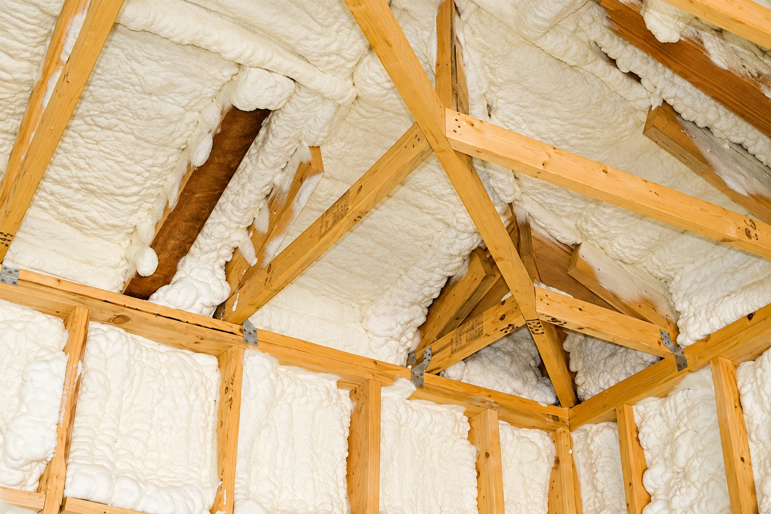 White spray foam insulation fills the spaces between exposed wooden rafters and framing.