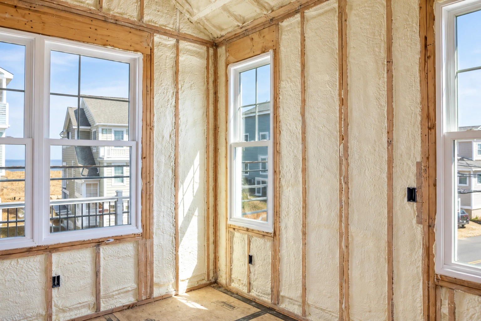 Wall insulation with cream-colored foam filling exposed wooden framing around several windows.